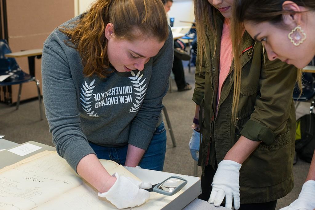 Students using a magnifying glass to look at historical U N E documents