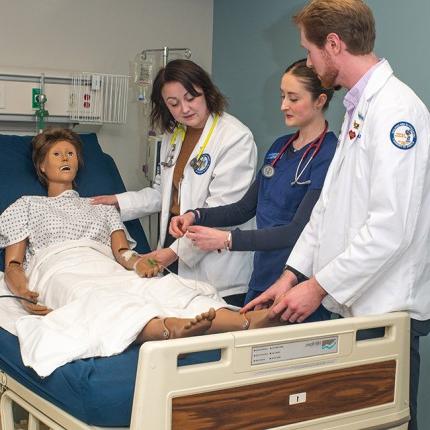 Three U N E students from different health majors work together on a dummy in the Simulation Lab