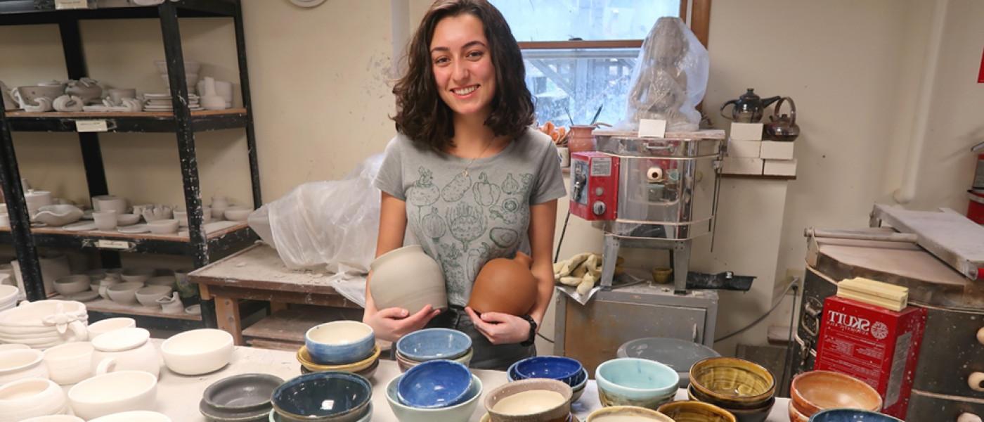 A U N E liberal arts student stands in front of a display of pottery she made in an arts class